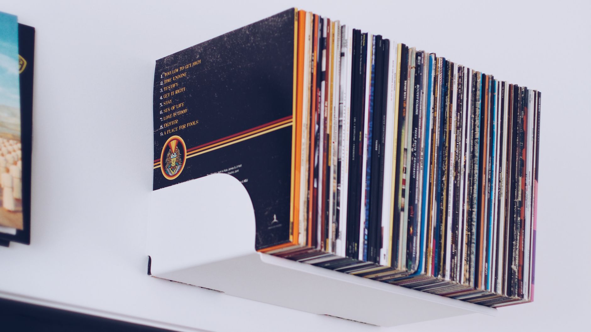 A neat stack of vinyl records on a minimalist white wall shelf.