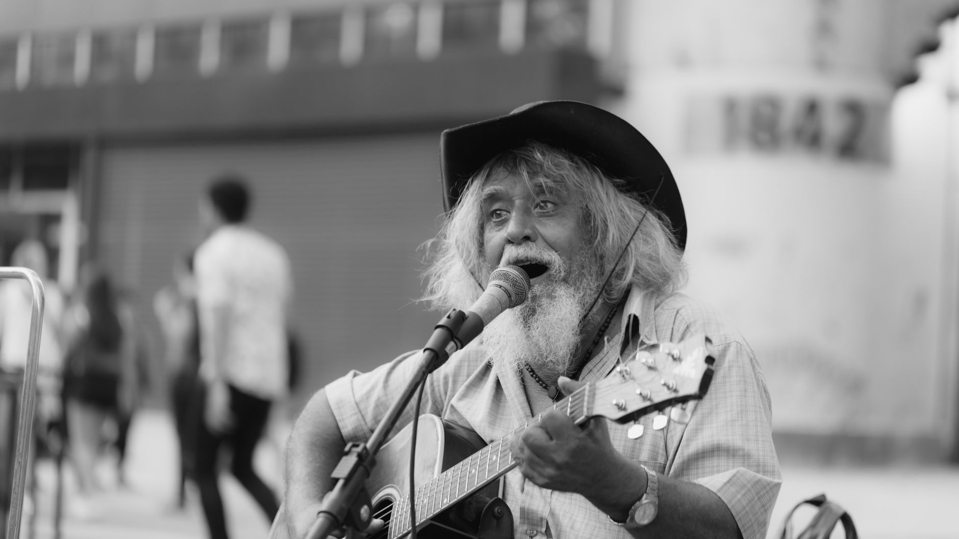 Foto en blanco y negro de un músico callejero mayor que canta y toca la guitarra.