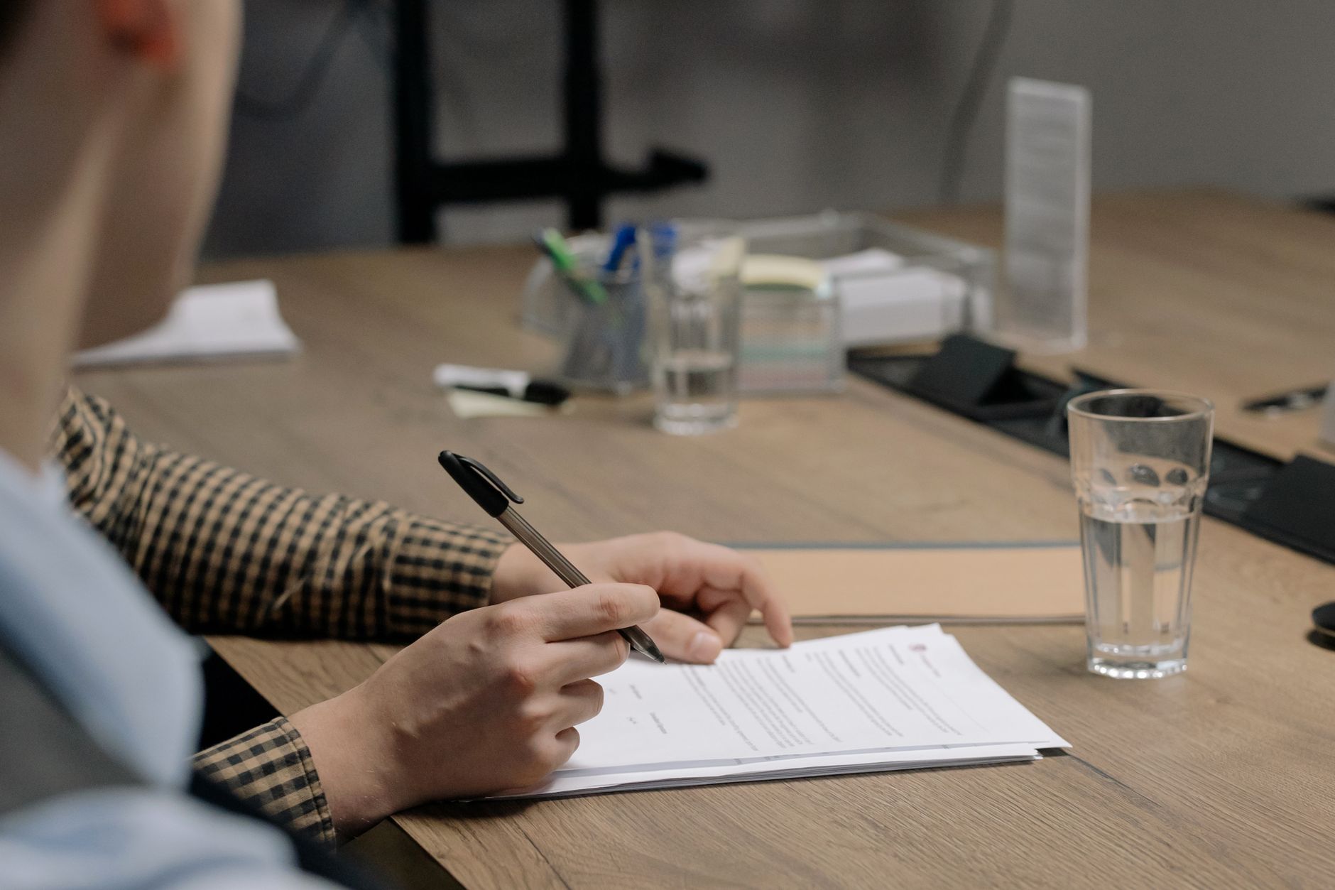 Persona con traje de negocios firmando un documento en una mesa de madera en una oficina.