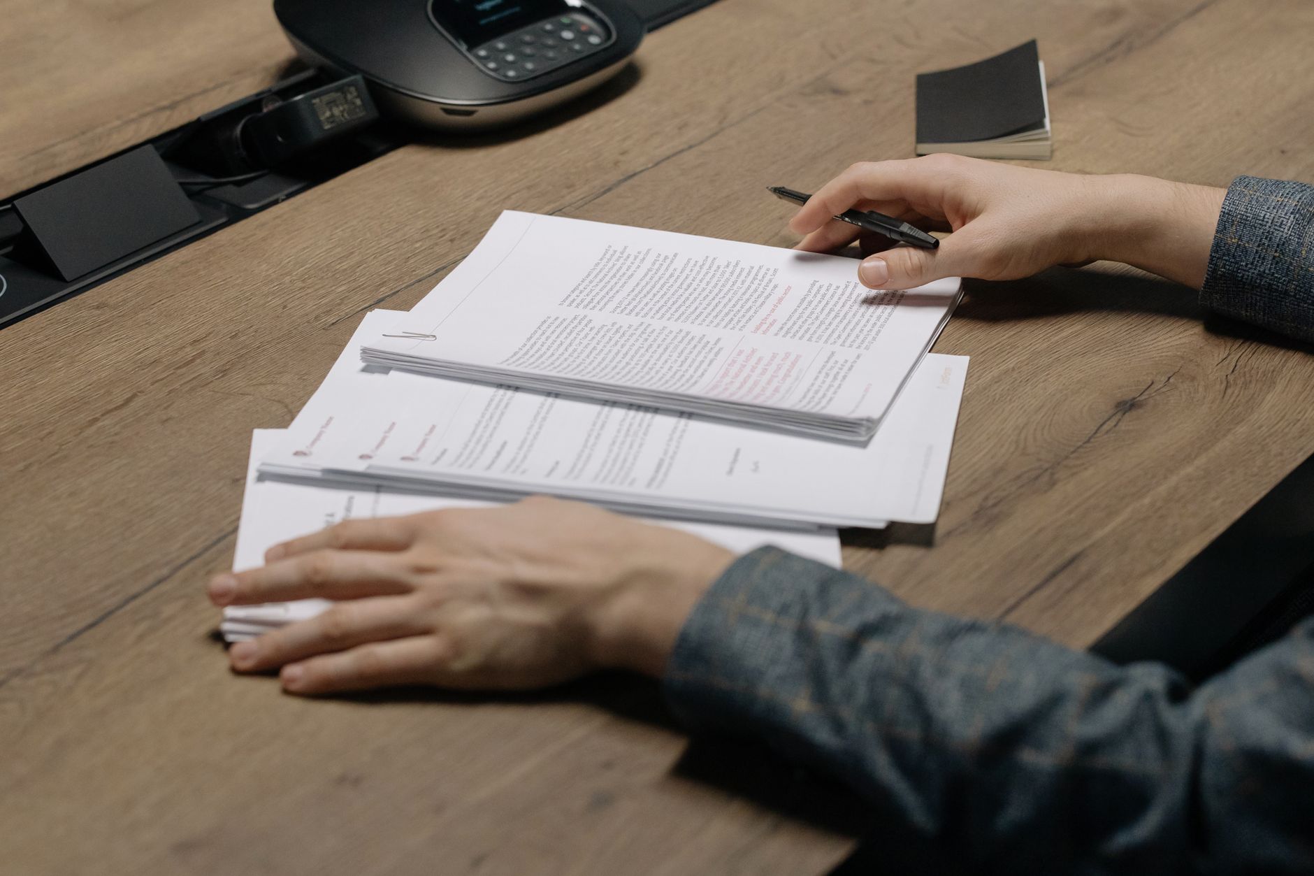 Primer plano de una persona revisando documentos con un bolígrafo en un escritorio moderno de oficina.