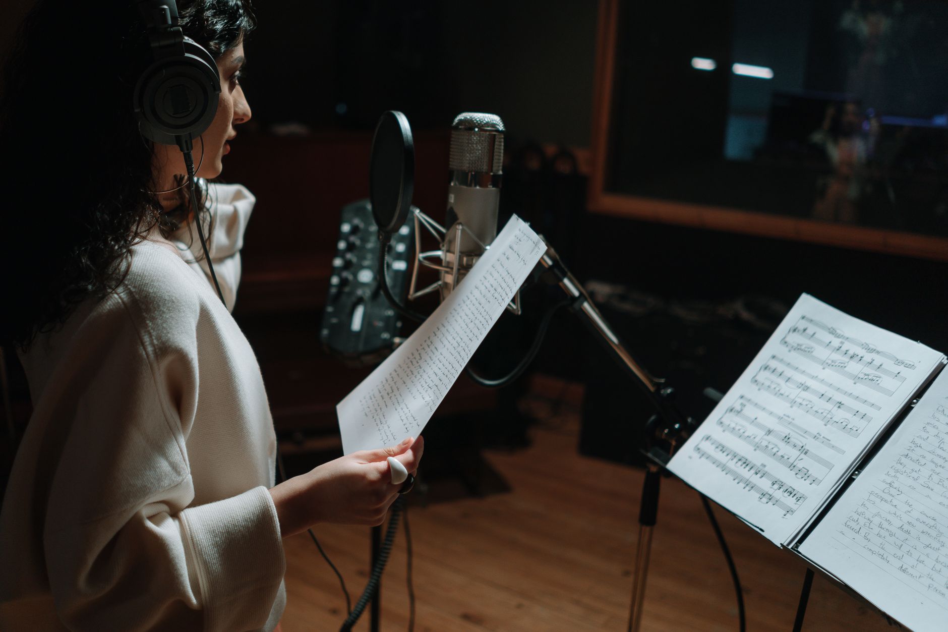 Woman in a music studio recording a song with a condenser microphone and headphones.