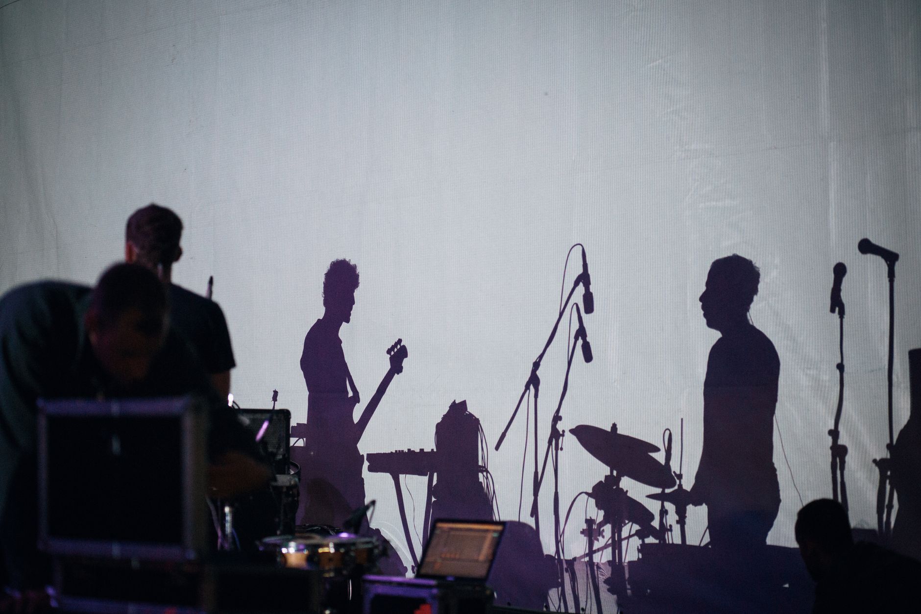 Siluetas de una banda tocando con instrumentos en un escenario, creando una atmósfera de concierto dinámica.