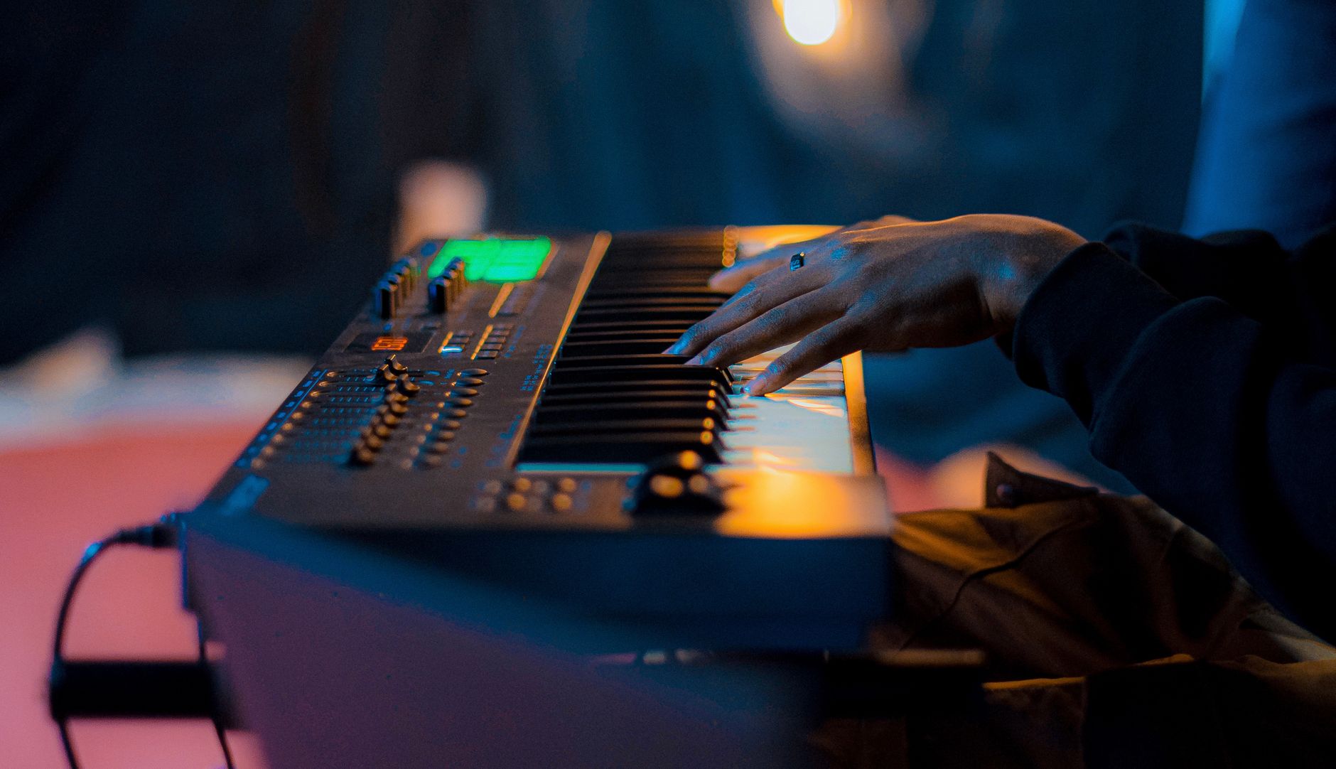 Primer plano de una mano tocando un teclado electrónico bajo una iluminación cálida.
