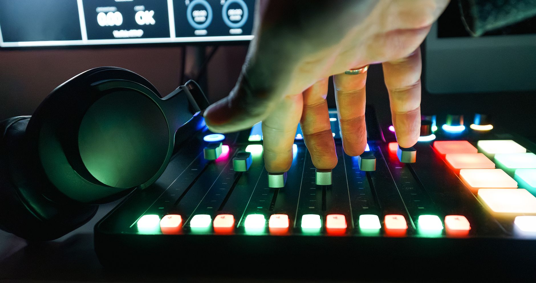 Close-up of a hand adjusting sliders on a colorful audio mixer, with headphones nearby in a recording studio.