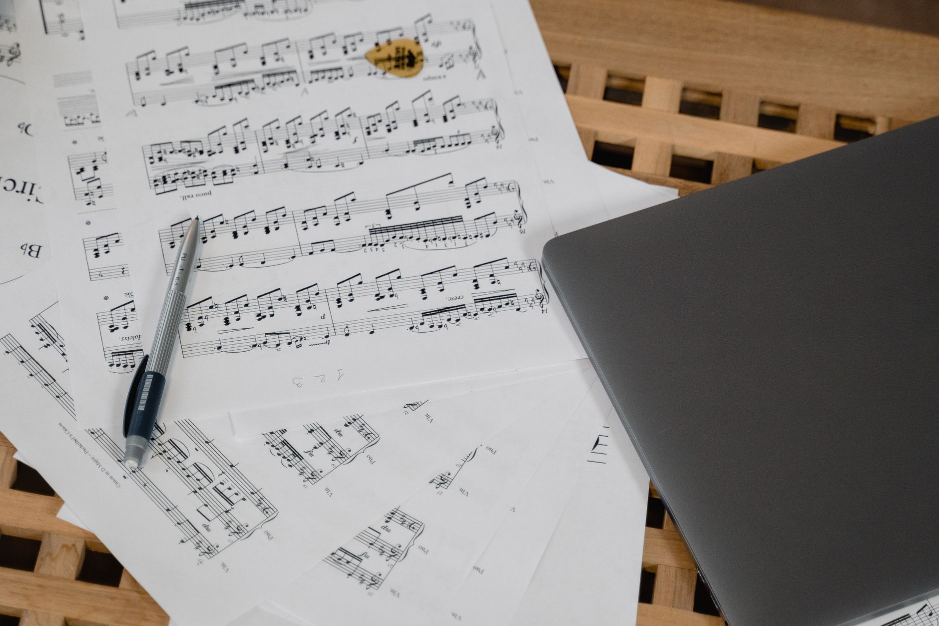 Primer plano de una composición musical con laptop y uña de guitarra sobre una mesa de madera.